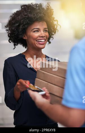 Une délicieuse pizza chaude est à payer. Photo d'une femme d'affaires heureuse acceptant une livraison de pizza d'un livreur non identifiable dans le bureau. Banque D'Images