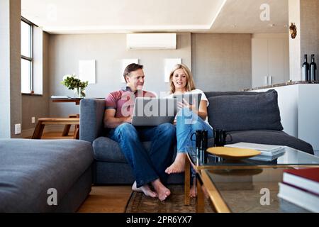 Faire leur propre chose... ensemble. Photo d'un couple d'âge mûr assis sur son canapé à l'aide d'un ordinateur portable et d'une tablette numérique. Banque D'Images