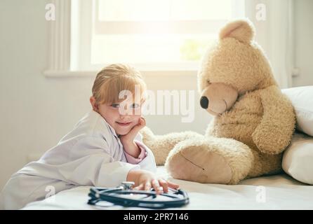 Je me suis mis à vous aider avec votre santé. Photo d'une adorable petite fille vêtue comme médecin et traitant son ours en peluche comme une patiente. Banque D'Images