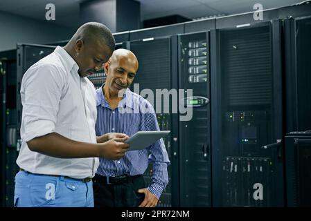 Pour chaque problème INFORMATIQUE, ils ont une solution. Photo de deux techniciens INFORMATIQUES utilisant une tablette numérique tout en travaillant dans un centre de données. Banque D'Images