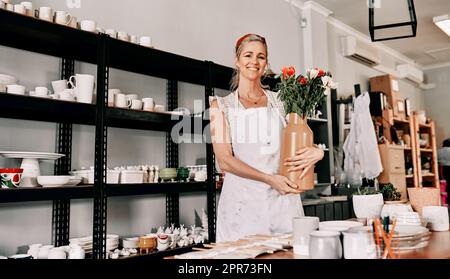 Je vends des vases aussi. Portrait rogné d'une belle femme mûre debout seule et tenant un vase fait main dans son atelier de poterie. Banque D'Images