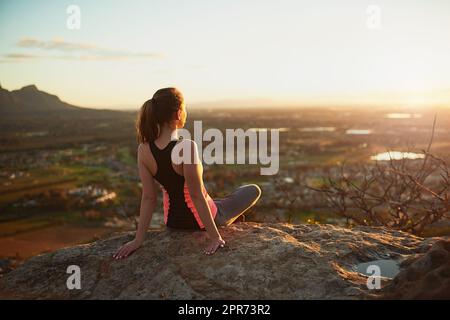 Quelle vue. Vue arrière d'une jeune femme sportive qui prend la vue lors d'une randonnée en haut de la montagne. Banque D'Images