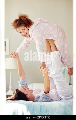 S'amuser au coucher. Prise de vue d'une jeune mère qui lève sa fille avec ses jambes tout en étant allongé sur le lit. Banque D'Images