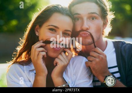 Nous vous moustaches si vous remarquez quelque chose de différent à notre sujet. Portrait d'un jeune couple qui profite d'un moment stupide ensemble tout en se liant à l'extérieur. Banque D'Images