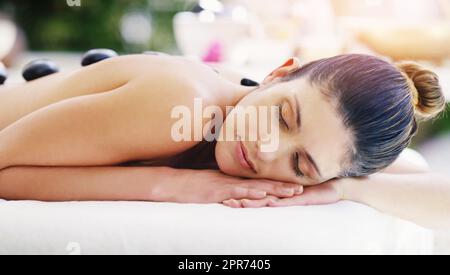 Je ne peux que me départir dans un état aussi magique. Photo d'une jeune femme recevant un massage aux pierres chaudes dans un spa. Banque D'Images