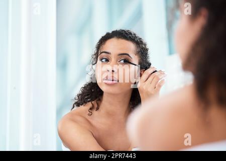 Ce n'est pas un bon jour jusqu'à ce que la mascara soit appliquée. Photo d'une belle jeune femme appliquant la mascara dans son miroir de salle de bains. Banque D'Images