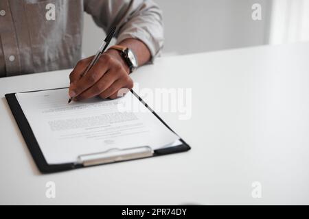 Signature de son contrat. Photo en grand angle d'un homme d'affaires méconnaissable remplissant un formulaire sur un presse-papiers tout en étant assis à son bureau dans le bureau. Banque D'Images