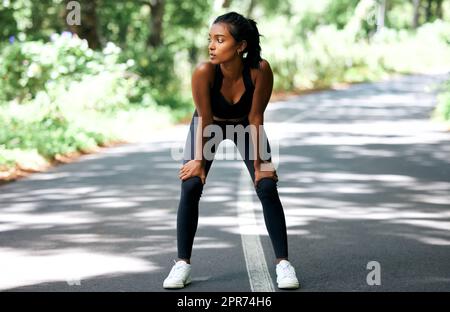 J'aime le sentiment de brûler des poumons pendant une course. Photo d'une jeune femme attirante prenant un moment pour prendre son souffle pendant sa course à l'extérieur. Banque D'Images