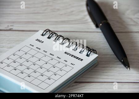 Calendrier de bureau blanc de novembre 2023 avec stylo noir sur table en bois. Banque D'Images