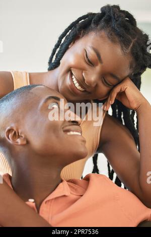 Jeune heureux joyeux couple afro-américain se liant et appréciant se détendre ensemble à la maison. Affectueuse femme noire souriant tout en embrassant et en regardant son petit ami assis ensemble et parlant Banque D'Images