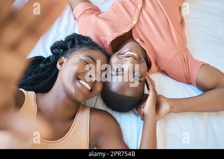 Portrait d'un jeune couple afro-américain heureux souriant et passant la matinée au lit ensemble. Couple affectueux noir prenant un selfie tout en regardant confortable et détendu dans un lit Banque D'Images