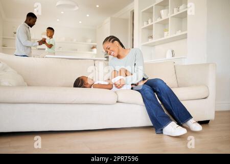 Jeune mère afro-américaine heureuse et joyeuse jouant et liant avec sa fille sur le canapé dans le salon à la maison. Femme noire jouant avec sa petite fille mignonne le week-end Banque D'Images