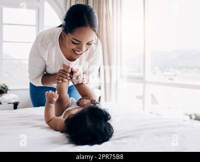 Modifions cette couche. Photo d'une jeune femme attrayante qui se joint à son bébé à la maison tout en changeant sa couche. Banque D'Images