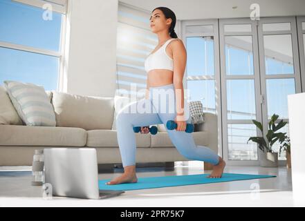 Je suis l'architecte de ma propre destinée. Photo d'une jeune femme sportive utilisant un ordinateur portable et faisant des fentes tout en s'exerçant à la maison. Banque D'Images