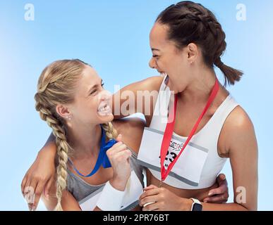 Deux femmes athlétiques gaies s'embrassant tout en tenant des médailles d'or de la compétition dans les événements sportifs. Une tenue joyeuse les athlètes actifs se sentent fiers après avoir remporté la course à pied. Les coureurs atteignent leur objectif Banque D'Images