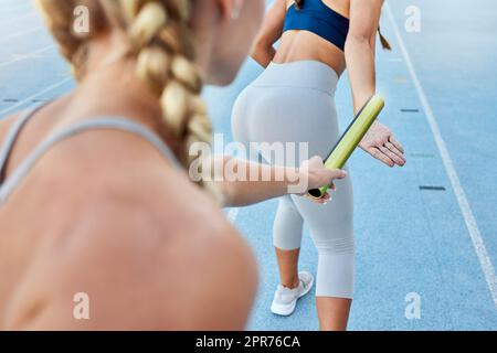 Un athlète de course de relais remet le bâton à un coéquipier tout en courant de derrière. Gros plan de deux athlètes féminins travaillant ensemble en équipe pour participer à une compétition sportive et gagner une compétition Banque D'Images