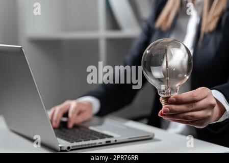 Femme d'affaires saisissant les dernières mises à jour sur le tour Haut sur le bureau tenant l'ampoule. Femme au bureau écrivant un message important sur un ordinateur. Executive Insertion de données de base dans un PC. Banque D'Images