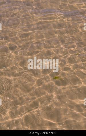 Nettoyer l'eau de la plage lors d'une journée d'été avec un espace de copie. Au-dessus de la vue de la mer calme marée basse ondule pendant le printemps. Gros plan de la lumière du soleil qui brille au large de l'océan peu profond utile comme un arrière-plan Banque D'Images