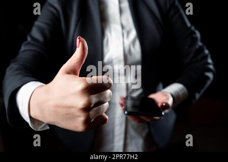 Femme d'affaires tenant un téléphone cellulaire et montrant le panneau OK. Femme ayant le téléphone d'une main et affichant des Thumbs Up avec l'autre. Dame avec tablette présentant un symbole avec un doigt. Banque D'Images