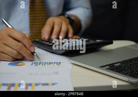 Homme d'affaires stylo à main avec graphiques et graphiques documents d'affaires calculatrice et ordinateur portable.financier et de marketing fiscal concept d'affaires. Banque D'Images