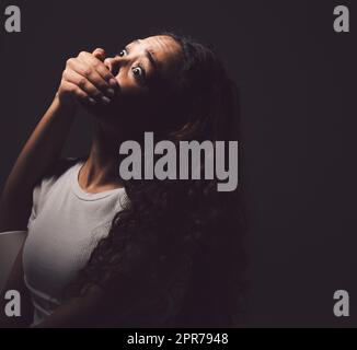 Un jour, vous raconterez votre histoire de la façon dont vous avez surmonté. Photo d'une bouche de jeunes femmes effrayée recouverte d'une main de homme méconnaissable sur un fond noir. Banque D'Images