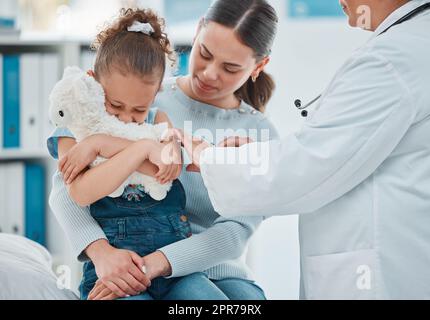 Une petite fille qui a peur de se faire mal a peur tout en obtenant une injection d'un médecin dans une clinique. Banque D'Images