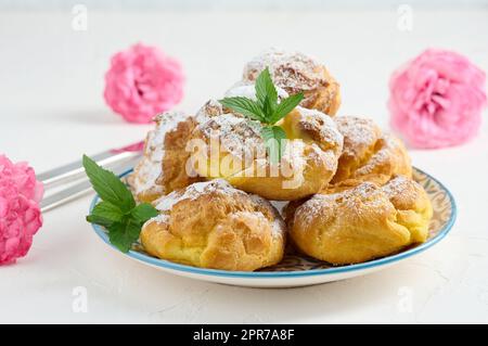 Eclairs cuits à la crème anglaise sur une plaque ronde en métal parsemée de sucre en poudre Banque D'Images