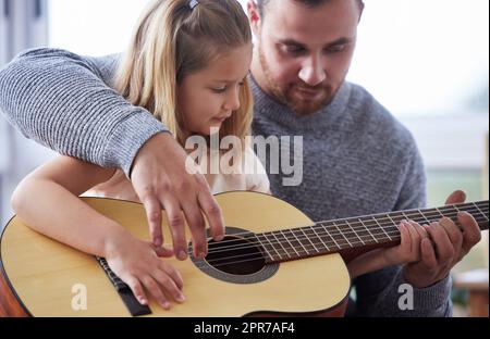 Le meilleur professeur qu'elle pourrait demander. Un jeune père enseignant à sa fille de jouer de la guitare à la maison. Banque D'Images