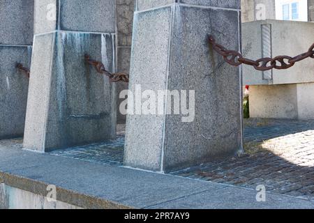 Gros plan de structures en béton sur la promenade par un port avec espace de copie. Chaînes rouillées accrochées entre des piliers de pierre sur un quai à l'extérieur. Une grande barrière entourant une surface de quai vivivirée à l'extérieur Banque D'Images