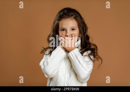 belle petite fille en chandail blanc en forme de curly demandant à être calme. Banque D'Images