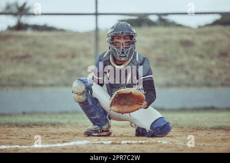 Portrait pichet afro-américain prêt à faire une prise avec un gant sur un terrain de baseball. Jeune sportif dans un casque prêt pour le ballon. Athlète d'homme noir jouant un jeu ou un match sur le terrain en plein air Banque D'Images