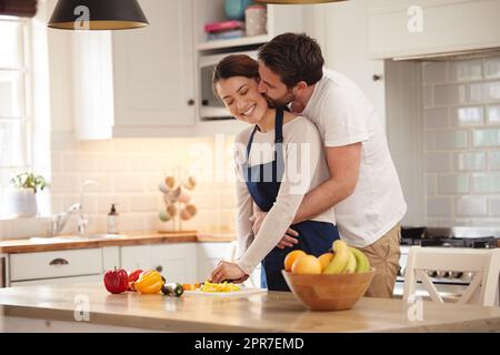 J'ai la meilleure femme au monde. Photo d'un homme qui embrasse sa femme pendant qu'elle prépare un repas dans la cuisine. Banque D'Images