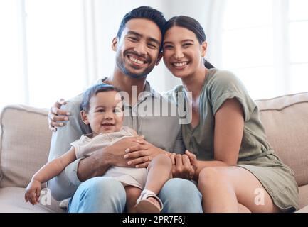 Sourit tout le monde. Photo d'un jeune couple qui se joint à sa petite fille sur un canapé à la maison. Banque D'Images