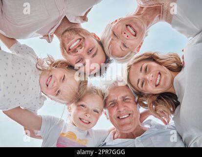 Photo ci-dessous d'une famille de plusieurs générations souriant dans un caucus contre le ciel bleu. Famille sans souci avec deux enfants, parents et grands-parents debout ensemble et regardant l'appareil photo Banque D'Images