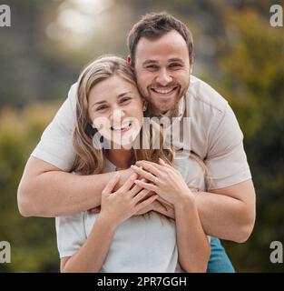 Portrait d'un jeune couple caucasien aimant passant du temps ensemble à l'extérieur par une journée ensoleillée. Beau homme souriant tenant et embrassant sa belle femme tout en se liant au parc. Banque D'Images