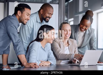 En train de tester sa présentation, un groupe diversifié de professionnels se sont rassemblés autour d'un ordinateur portable lors d'une réunion dans la salle de conférence. Banque D'Images