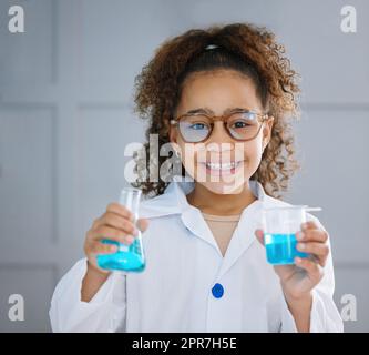 Comment réagiriez-vous ? Portrait court d'une adorable petite fille portant un manteau de travail tout en tenant deux contenants de liquide bleu. Banque D'Images