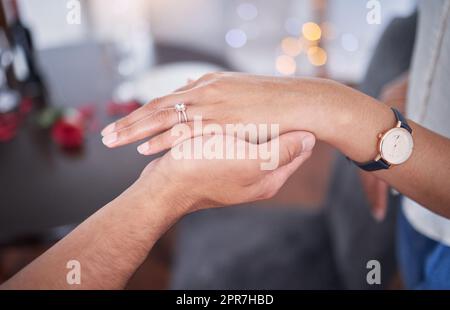 Notre toujours commence aujourd'hui. Un homme méconnaissable mettant une bague sur le doigt de ses amies à la maison. Banque D'Images