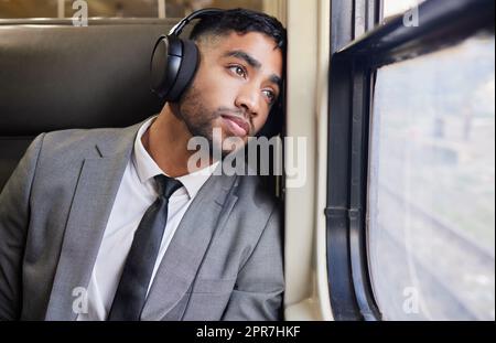 Dans une profonde contemplation lors de ses déplacements, un jeune homme d'affaires portant un casque tout en regardant par la fenêtre sur un train pendant ses trajets. Banque D'Images