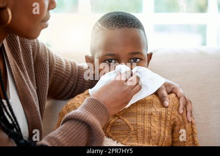 Une jeune mère qui aide son fils à souffler le nez à la maison, vous ramène à la santé. Banque D'Images