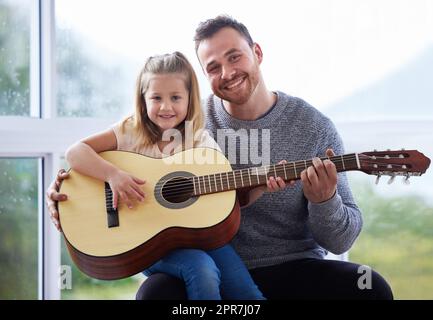 Shes une princesse parce qu'elle papas un roi. Un jeune père enseignant à sa fille de jouer de la guitare à la maison. Banque D'Images