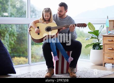 Derrière chaque douce fille se cache un père incroyable, un jeune père enseignant à sa fille de jouer de la guitare à la maison. Banque D'Images