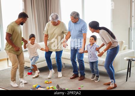 Famille de race mixte s'amusant et dansant dans le salon à la maison. Petits garçons et grands-parents ayant une journée de plaisir à la maison avec leurs parents. Avoir la bataille de danse avec la famille amusante Banque D'Images