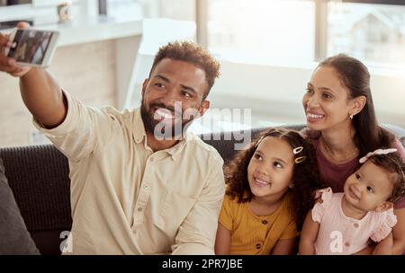 Des parents souriants de race mixte emmenaient un selfie sur un téléphone portable avec des filles adorables. Un homme hispanique heureux qui prend en compte la famille dans les médias sociaux sur la technologie. Mère, père et petites filles prenant des photos Banque D'Images