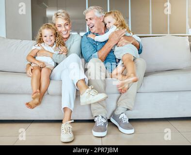 Un heureux couple d'âge mûr caucasien se liant avec leurs enfants d'accueil dans le salon. Deux sœurs se détendent avec leurs grands-parents sur un canapé pendant qu'elles aiment la garde d'enfants de deux adorables filles Banque D'Images