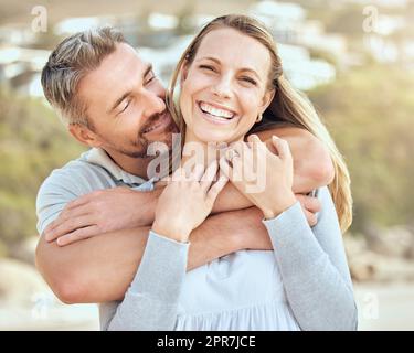 Un couple caucasien mature heureux et aimant appréciant une date romantique à la plage ensemble par une journée ensoleillée. Gai affectueux mari embrassant le bras autour de la femme tout en se liant sur les vacances à l'extérieur Banque D'Images