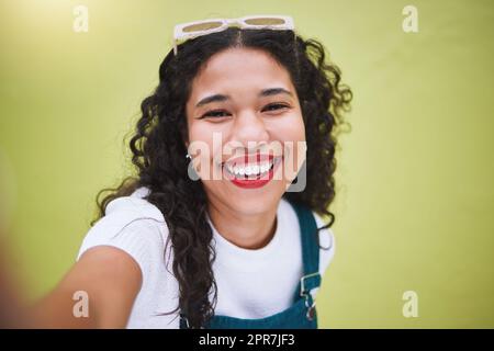 Gros plan magnifique femme de mode de course mixte prenant des photos de selfies sur un fond de mur vert lime dans la ville. Jeune femme hispanique heureuse à la fois élégante et tendance. Insouciant et tendance Banque D'Images