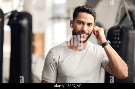 Portrait d'un jeune homme hispanique confiant qui écoute de la musique avec des écouteurs Bluetooth sans fil pour rester motivé tout en faisant de l'exercice dans une salle de sport. Happy Fit mixte race gars se préparer à l'entraînement avec ses chansons préférées sur une liste de lecture Banque D'Images