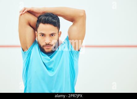 Portrait du joueur de squash s'étirant et regardant focalisé avant de jouer au jeu de terrain avec l'espace de copie. Mettez en forme un athlète hispanique actif seul et préparez-vous à l'entraînement dans un centre sportif Banque D'Images