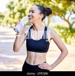 Une jeune femme de course mixte en forme de femme prenant une pause pour boire de l'eau de la bouteille tout en faisant de l'exercice à l'extérieur. Bonne athlète féminine qui se désaltérant et se rafraîchi après la course à pied et l'entraînement Banque D'Images